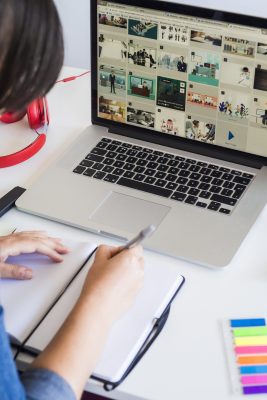 woman-taking-notes-near-laptop-headphones-table-min